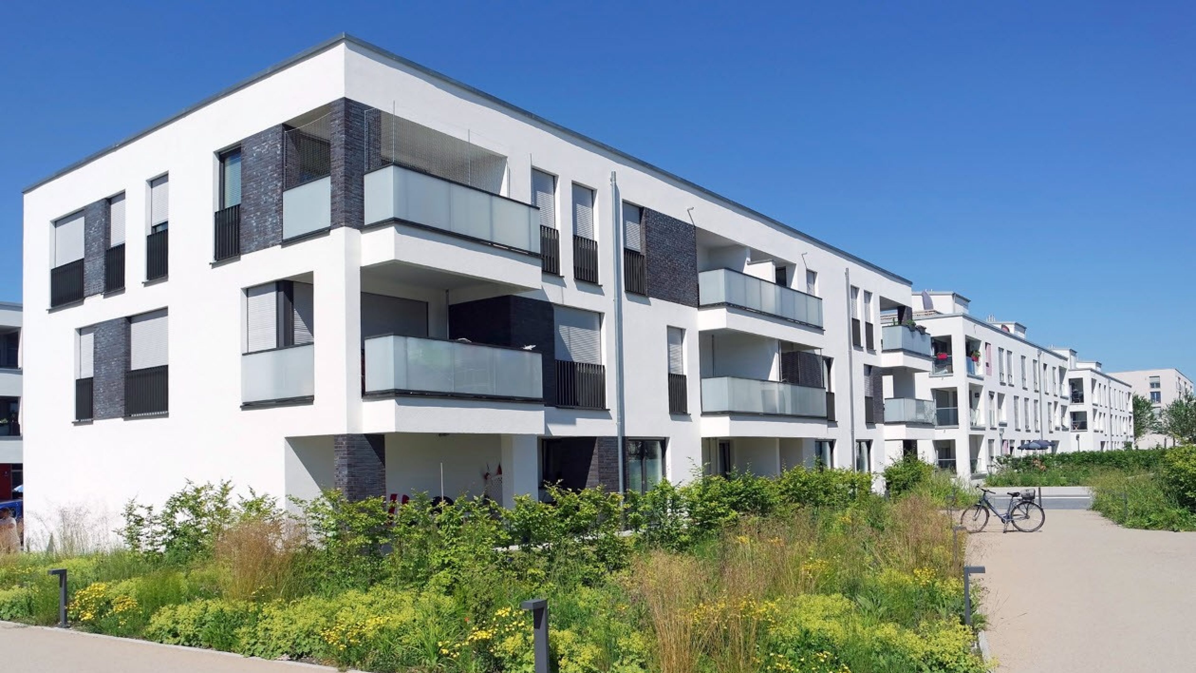 Moderne Mehrfamilienhäuser umgeben von Grünflächen und blauem Himmel.