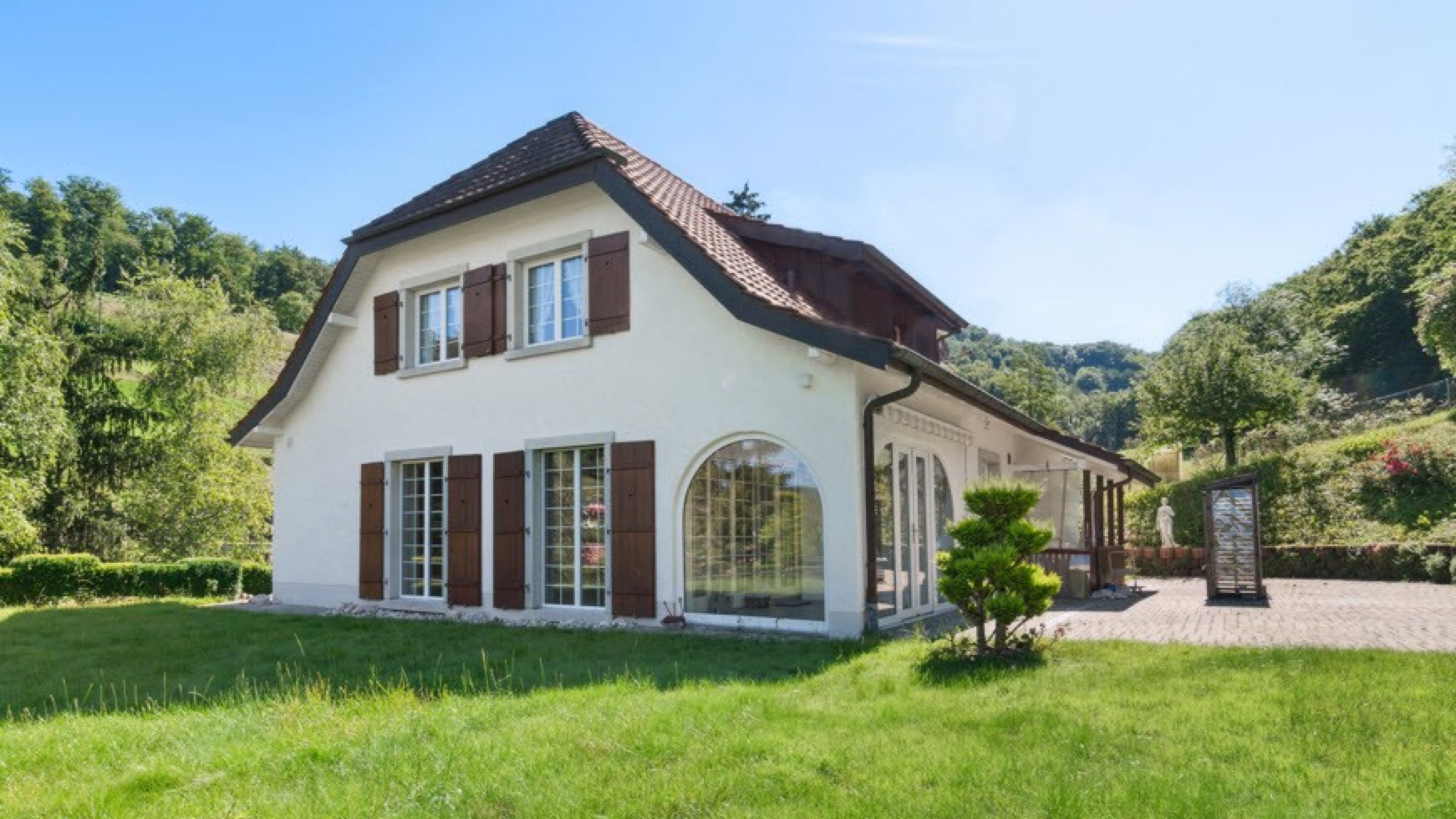 Einfamilienhaus mit braunen Fensterläden, umgeben von grüner Natur