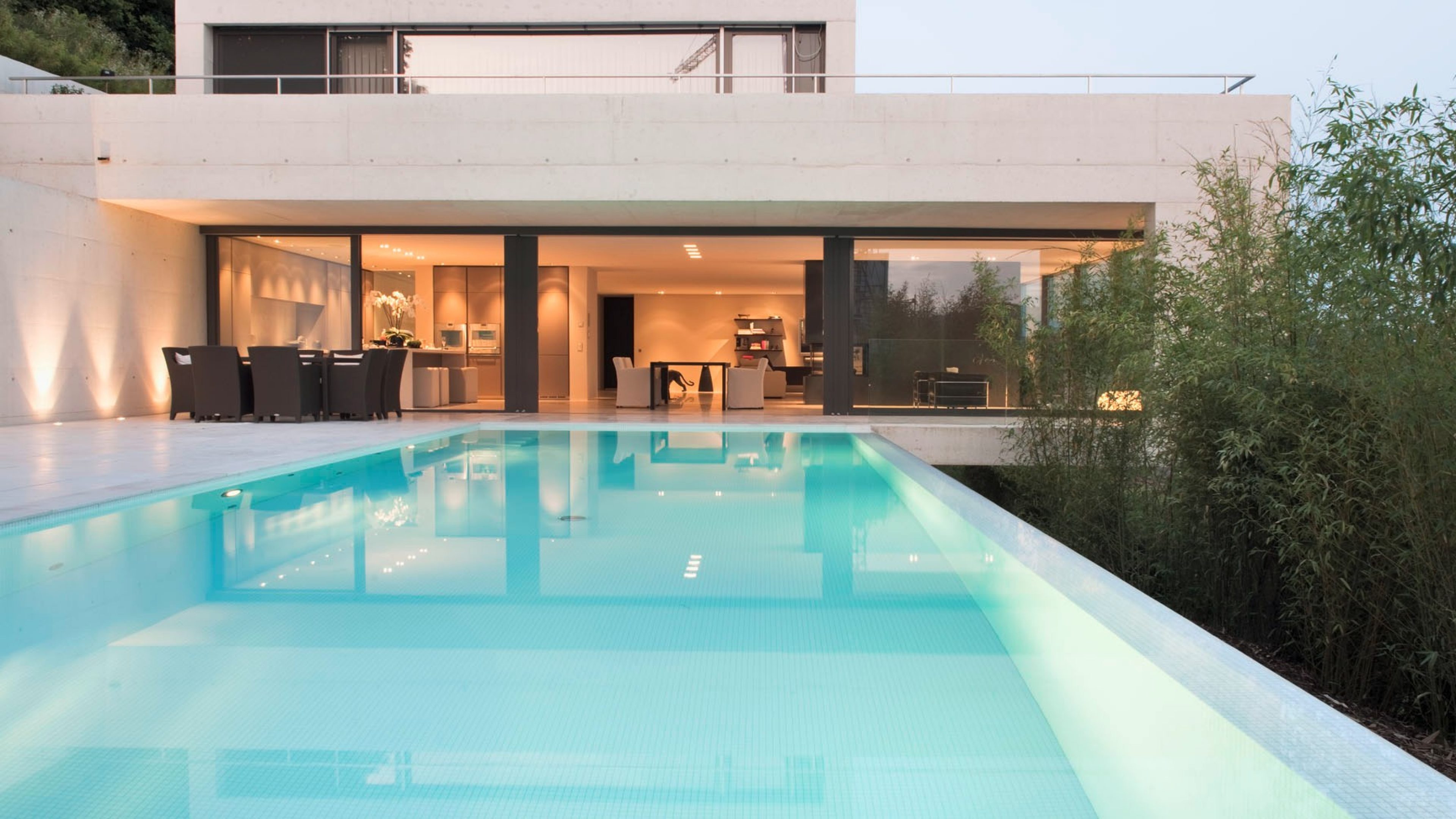 Luxus-Terrassenwohnung mit beleuchtetem Pool und Sicht ins hoch moderne und schlicht eingerichtete Wohnzimmer. 