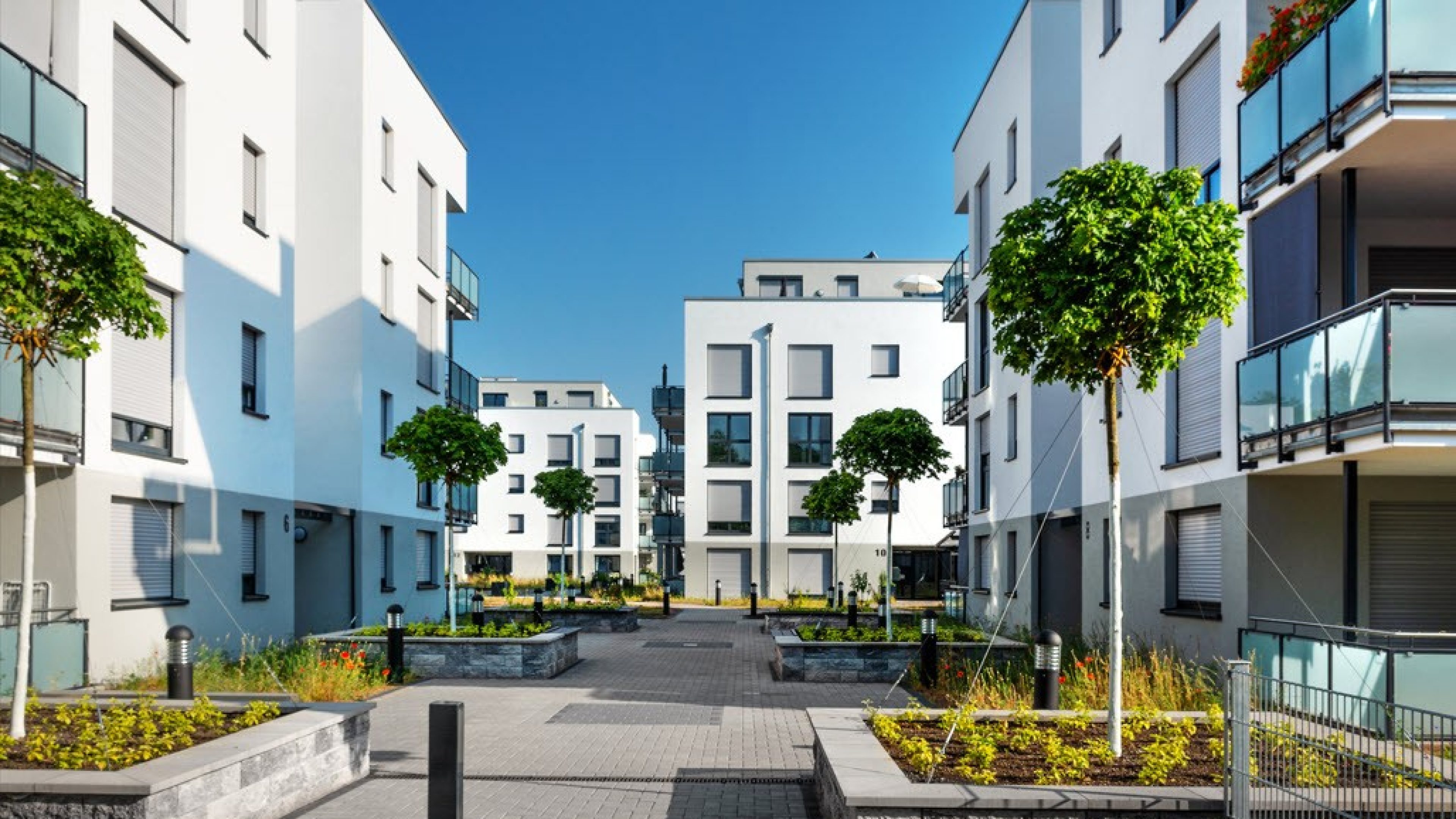 Moderne case plurifamiliari circondate da piante e cielo blu.
